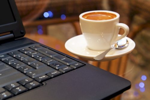 A black laptop sitting on a table next to a mug full of coffee