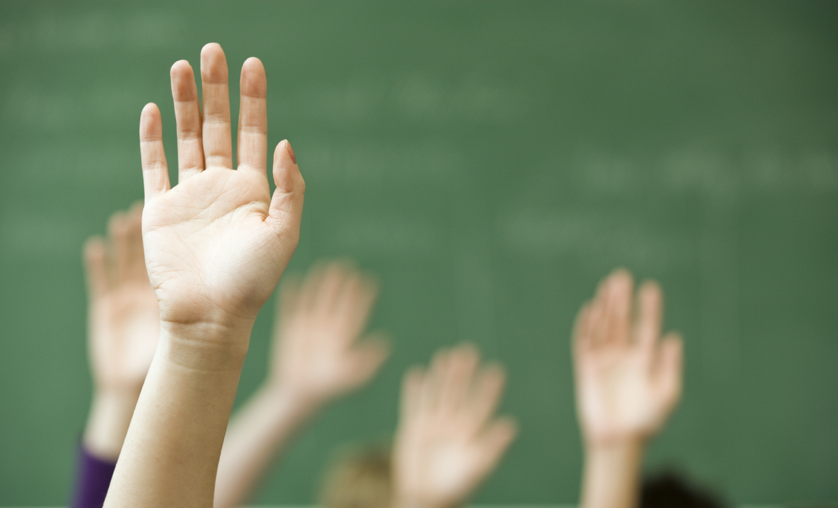 Hands raised in front of a green chalkboard