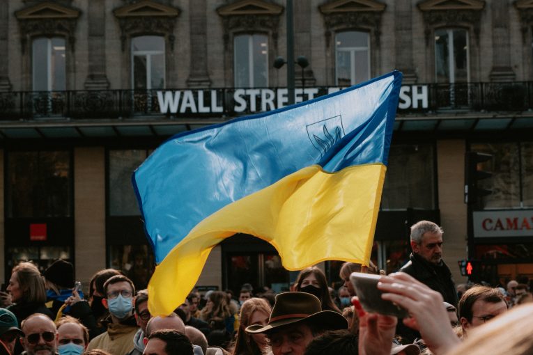 Ukranian flag above a crowd of people waves in front of Wall Street