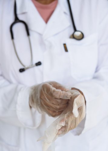 A blurred image of a person in a white lab coat with a stethoscope putting on plastic gloves